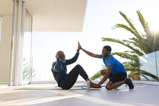 Exercising African American father and son doing sit-ups on terrace, with yoga mats, water bottle