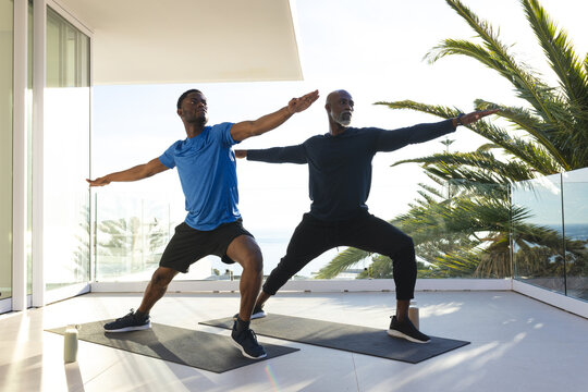 Practicing African American father and son holding Warrior II pose on balcony, with water bottle