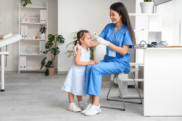 Fototapeta premium Female pediatrician with infrared thermometer measuring little girl's temperature in clinic