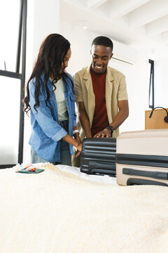 Packing African American couple loading suitcases in bedroom, with sunglasses and smartphone