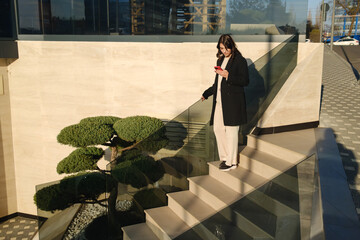 Businesswoman checking phone while walking downstairs in a contemporary architectural setting