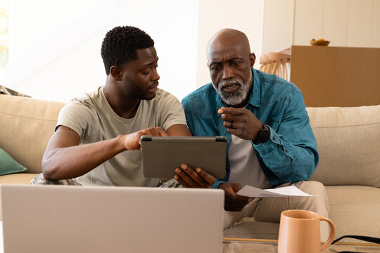 Comparing African American family studying documents and tablet in living room with cardboard boxes