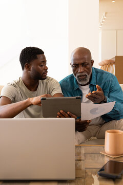 Discussing African American father and son reviewing tablet and chart on sofa in modern living room