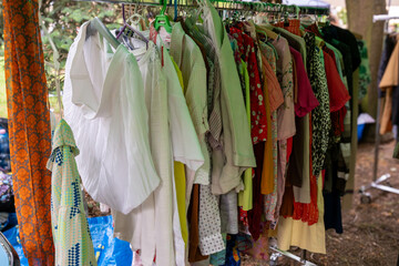 Soft colored secondhand tops on hangers in natural park background during reuse and swap fair