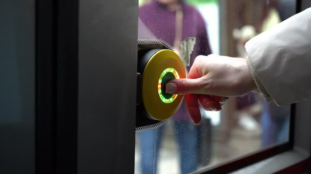 Close-up of a woman pressing a button to open transport doors. Urban commuting moment highlighting interaction with public transit and daily travel routine.

