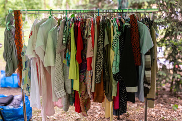 Bright and light summer shirts and blouses in pastel tones on metal rack under trees during eco event