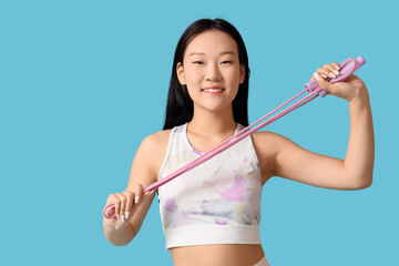 Sporty young Asian woman with skipping rope on blue background