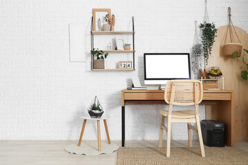 Comfortable workspace with modern computer and houseplants near white brick wall