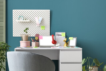 Stylish workspace with modern laptop, headphones and colorful sticky notes near blue wall