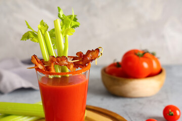 Glass of bloody mary cocktail with bacon and celery on grey background