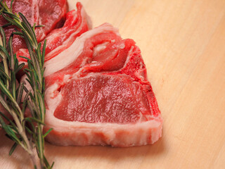 Fresh lamb loin chops and fresh green rosemary herb on a wooden board. Expensive high quality meat product with bone for frying. Butcher craft display.