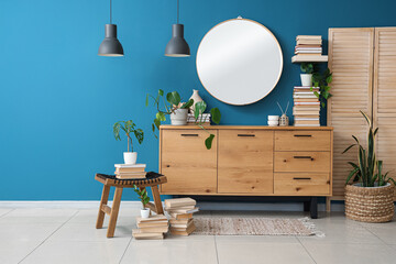 Chest of drawers with books, coffee table and mirror on blue wall in room