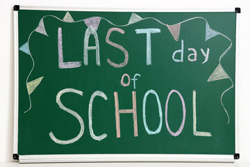 Blackboard with text LAST DAY OF SCHOOL and drawn flags on light wall