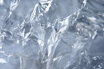 Crinkled cellophane texture with glossy surfaces in shades of grey and translucent highlights creating an abstract