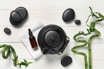 Composition with teapot, bottle of essential oil, spa stones and bamboo stems on light wooden background
