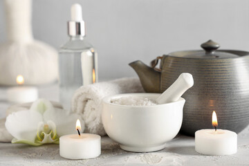 Composition with spa accessories, cosmetics, teapot and burning candles on light table