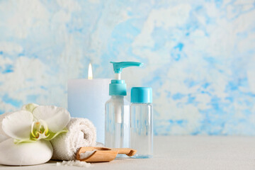 Composition with spa accessories, cosmetic products and burning candle on light table near color wall