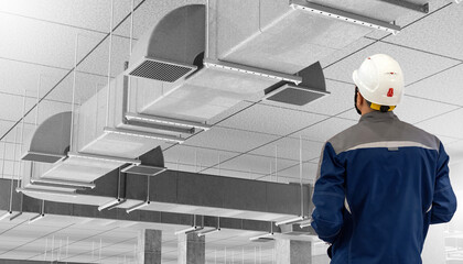 Technician in uniform and hard hat inspects ceiling ventilation and ductwork in a commercial building. Activity: HVAC. Construction. Engineering.