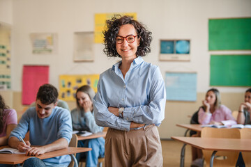 A mature female teacher stand confidently in her elementary classroom