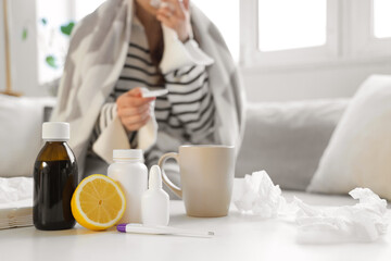 Different flu medications with lemon on table against sick woman at home, closeup