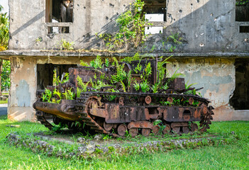 Rusted Japanese tank from World War II, now overtaken by tropical plants, sits abandoned in front of the bomb-damaged Japanese Communications Center in Palau. The fusion of corroded steel and vibrant