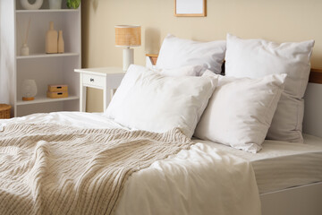 Cozy bed with soft pillows and beige blanket in light bedroom, closeup