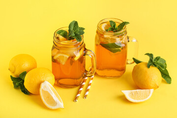 Mason jars of lemon ice tea with mint and citrus fruits on yellow background