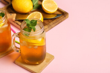 Mason jars of lemon ice tea with mint on pink background, closeup