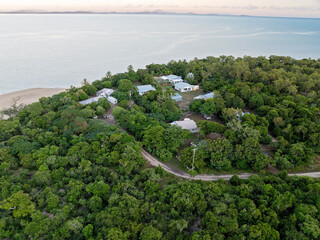 Aerial coastal settlement with houses and gardens nestled in dense forest by the ocean.