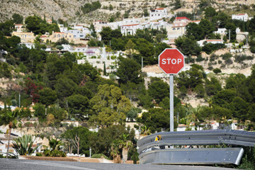 Stop sign and curved guardrail on mountain road with scenic hillside houses