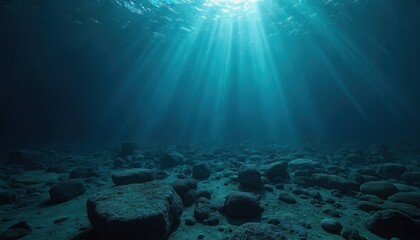 Sunlight streams illuminate deep ocean rocky seabed. Sunbeams create mysterious underwater effect. Rocks, stones on ocean floor, water surface, aquatic nature scene. Tranquil, calm environment.