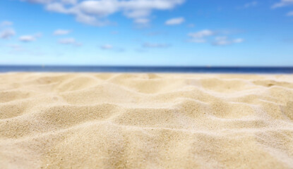Beach Sand Close-Up with Copy Space – Summer Background for Product Placement. Sunlit beach sand with soft focus blue sea and sky in the background