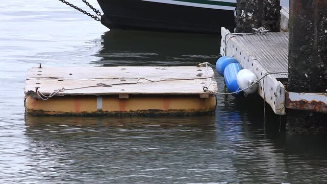 Small Floating Squre Attached To A n Ocean Pier With A Partial Hull In The Background