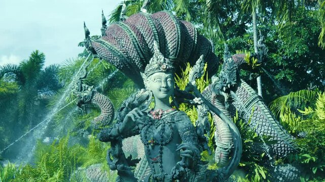 Stone statues of Garuda and Naga are standing in the green garden of Erawan, Thailand. Shot in motion