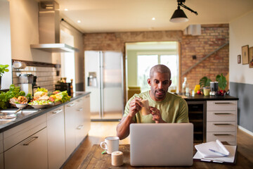 Middle aged african american food blogger and nutritionist promoting a health supplement and vitamin pills or tablets to his audience over a stream or video call on his laptop in the kitchen