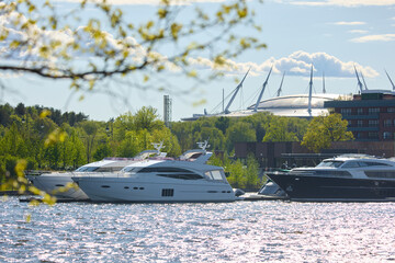 View of the mega yachts standing at the pier through the branches of trees on a clear sunny day,...