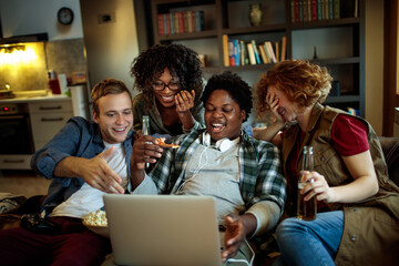 Young and diverse group of friends watching a movie on laptop in the living room on the couch
