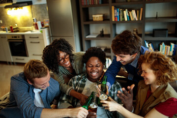 Diverse group of friends laughing and toasting with beer bottles at home party gathering
