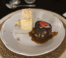 Gourmet gastronomy in a social event. Closeup view of a grilled loin fillet with sauce and a potato mille feuille in a white dish on the gala table	
