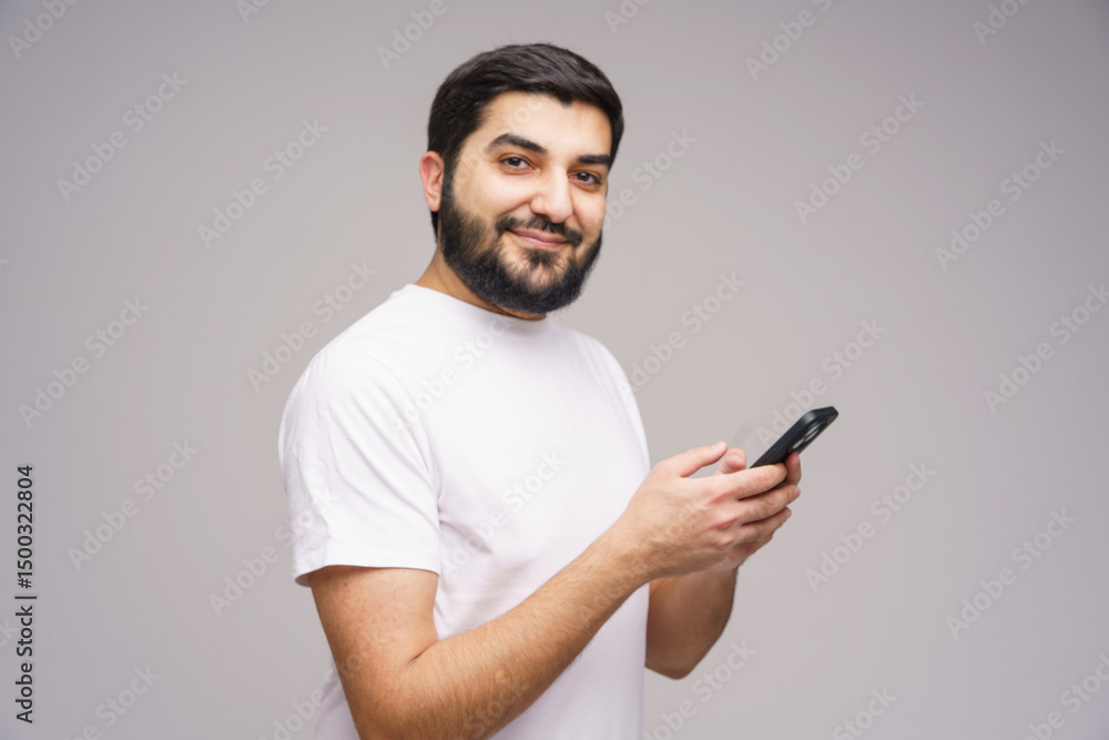 Fototapete smiling young man engages with smartphone, capturing modern connection in a minimalist setting
