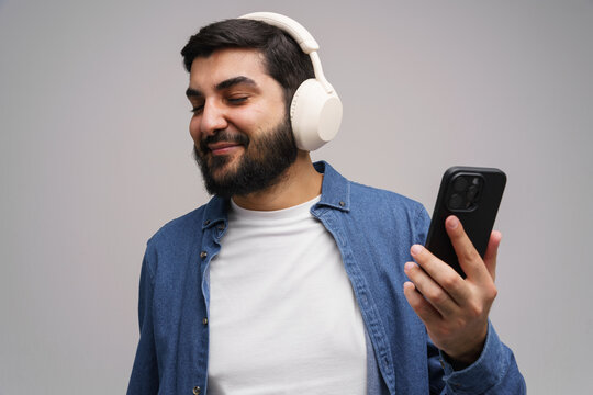 Young man enjoys music with wireless headphones while holding smartphone in a cozy atmosphere