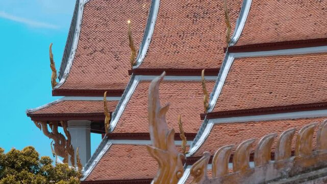 Red tiles with golden serpent-shape chofahs on the roof of traditional Thai temple. Shot in motion