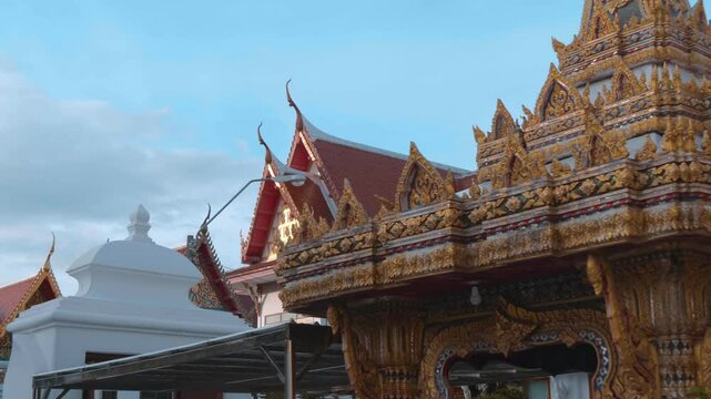 Roofs of traditional Thai style paved with orange tiles, gold carved chofas and the bell tower of the Buddhist Temple in Bangkok. Shot in motion