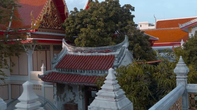 Roofs of traditional Thai style paved with orange tiles and gold carved chofas of the Buddhist Temple in Bangkok. Shot in motion