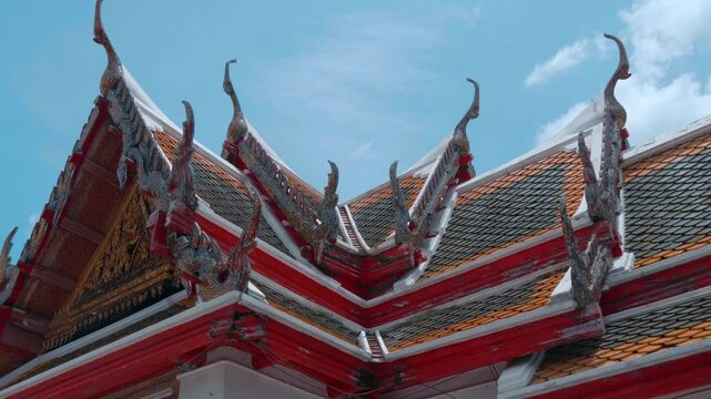 Traditional Lai Thai style orange and blue tiled roof with massive Chofahs (serpent-like edges) and ornate golden carvings of a Buddhist temple in Bangkok. Shot in motion