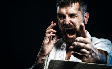 Strong karate man in kimono shows kick by hand. Karate master preparing for competition. Selective focus. Screaming karate man breaks concrete brick. Karate fighter smashes concrete slab. Copy space.
