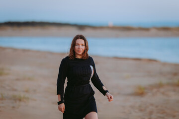 Woman in black dress walking on the beach at sunset