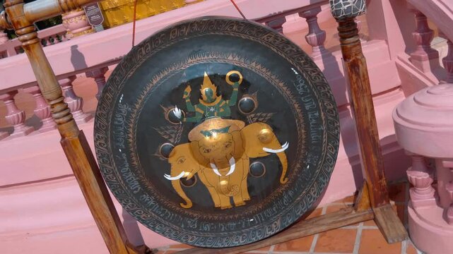 A black gong with a picture of God Indra on his mount - Three-headed Elephant Erawan and a mallet are situated near the ancient stupa. Shot in motion