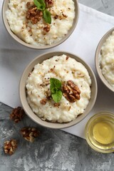 Delicious rice pudding with walnuts, mint and honey on grey table, flat lay