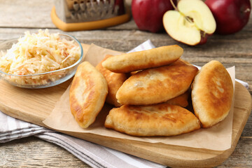 Delicious fried pyrizhky (stuffed pies) and apples on wooden table, closeup